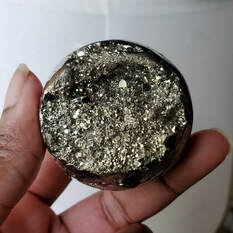 A pyrite sphere being held for viewing.
